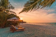 Sun setting over a beach with lounge chairs and beach umbrella