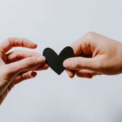 two hands reaching for a paper heart support and connection